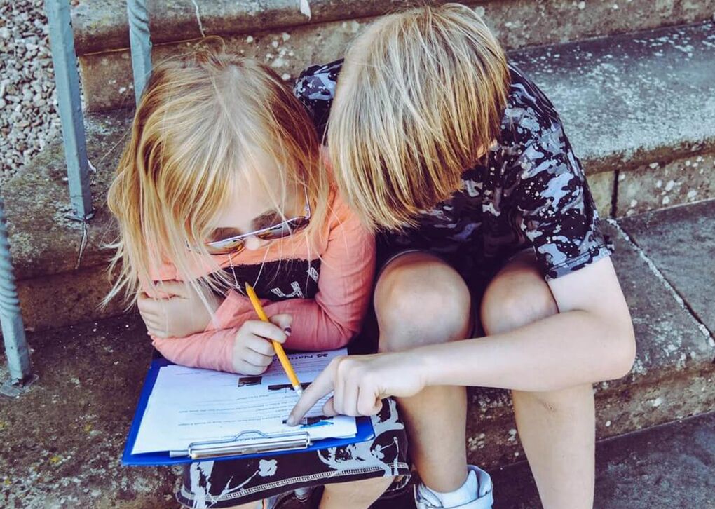 Zwei Kinder sitzen auf Treppenstufen und studieren gemeinsam ein Blatt Papier. Eines von ihnen hält einen Bleistift und zeigt auf etwas.
