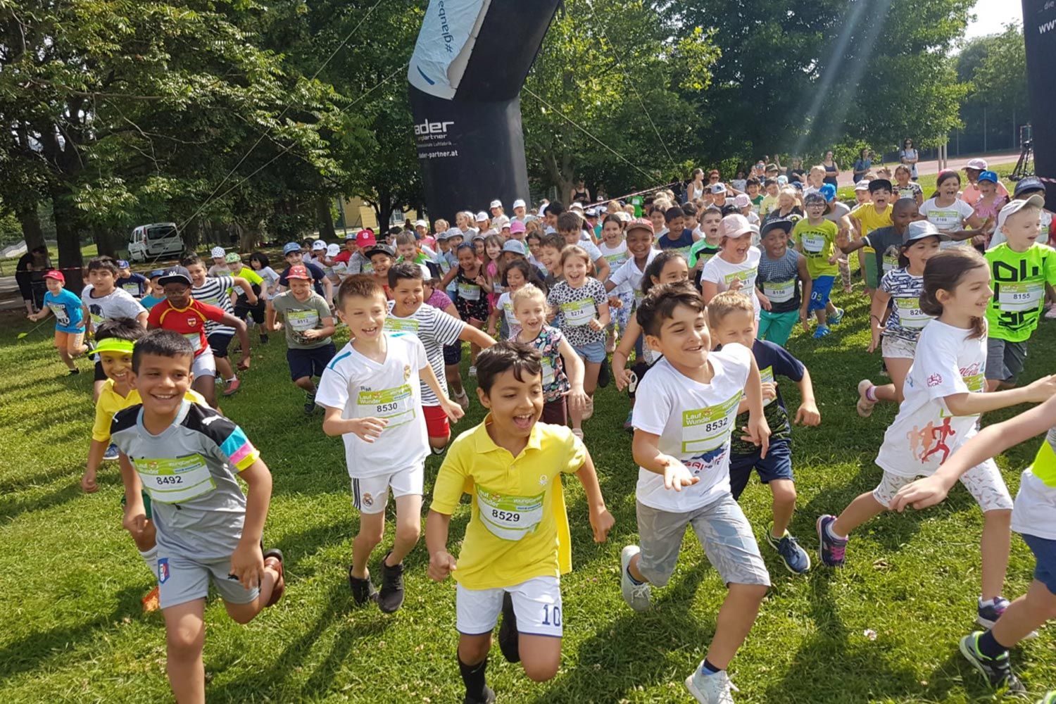Eine Gruppe von fröhlichen Kindern, die in einem Park an einem Rennen teilnehmen, tragen T-Shirts mit Nummern und genießen den sonnigen Tag.