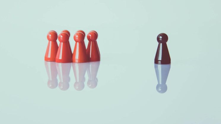 Rote Spielfiguren stehen zusammen, während eine schwarze Figur alleine ist, was Isolation oder Ausgrenzung symbolisieren könnte.