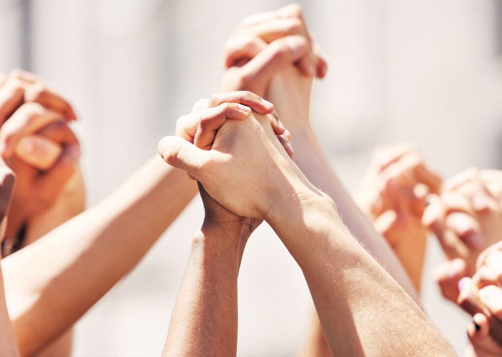 Eine Gruppe von Menschen hält ihre Hände hoch, um Unterstützung und Einheit zu zeigen. Die verschiedenen Hauttöne symbolisieren Vielfalt.