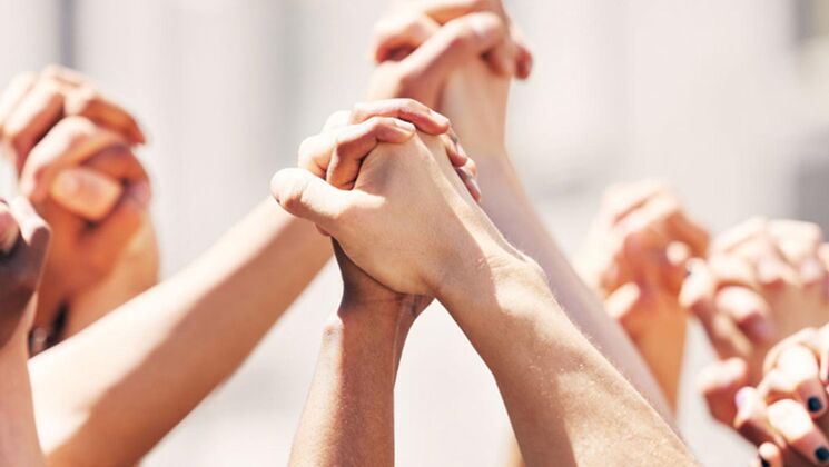 Eine Gruppe von Menschen hält ihre Hände hoch, um Unterstützung und Einheit zu zeigen. Die verschiedenen Hauttöne symbolisieren Vielfalt.