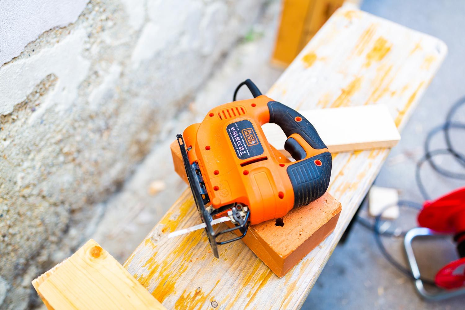 Eine orange Elektro-Säge liegt auf einem Holzbrett, umgeben von Werkzeug und Materialien auf einer Arbeitsfläche.