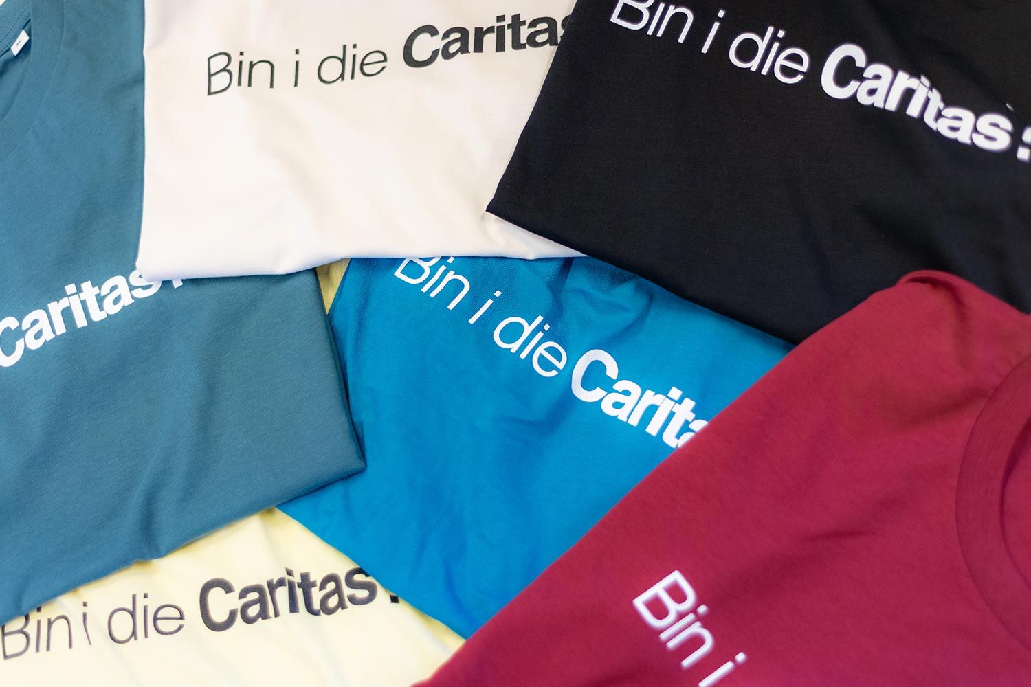 Sechs unterschiedlich gefärbte youngCaritas-T-Shirts gefalten
