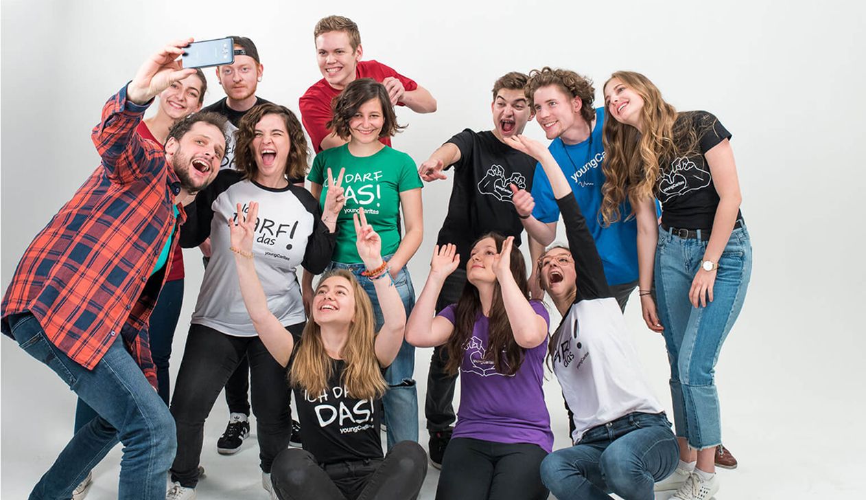 Gruppe junger Menschen, die fröhlich in die Kamera lächeln und hoch die Hände halten, während sie ein Selfie machen
