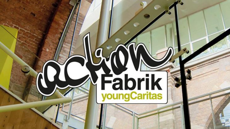 Logo von Aktion Fabrik - youngCaritas vor einer modernen, hellen Architektur mit Fenstern und Holzstufen.
