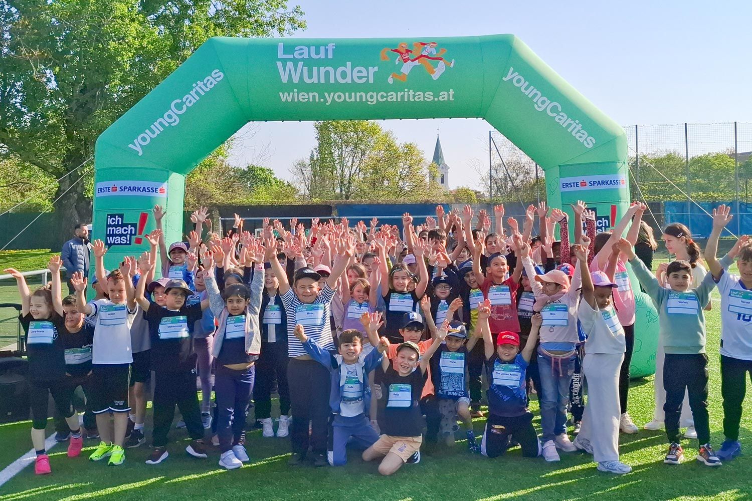 Gruppenfoto von Kindern, die beim Lauf Wunder-Event in Wien mit erhobenen Händen feiern, unter einem großen grünen Bogen.