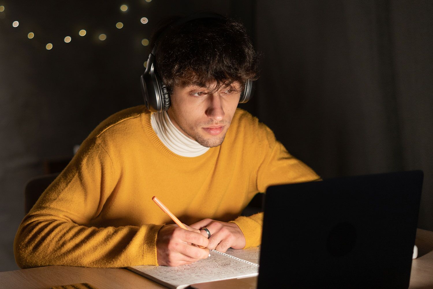 Junger Mann mit Kopfhörer am Kopf lernt vor dem Laptop im Dunkeln