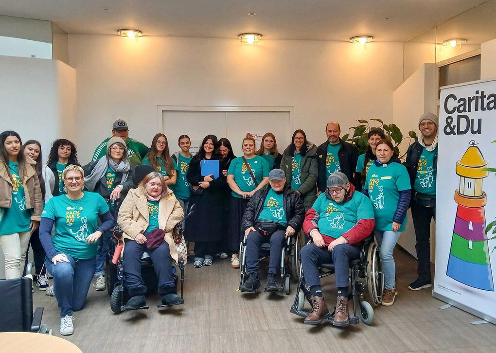 Eine Gruppe von Freiwilligen in grünen T-Shirts posiert in einem Raum für ein Gruppenfoto, während sie sich engagieren.